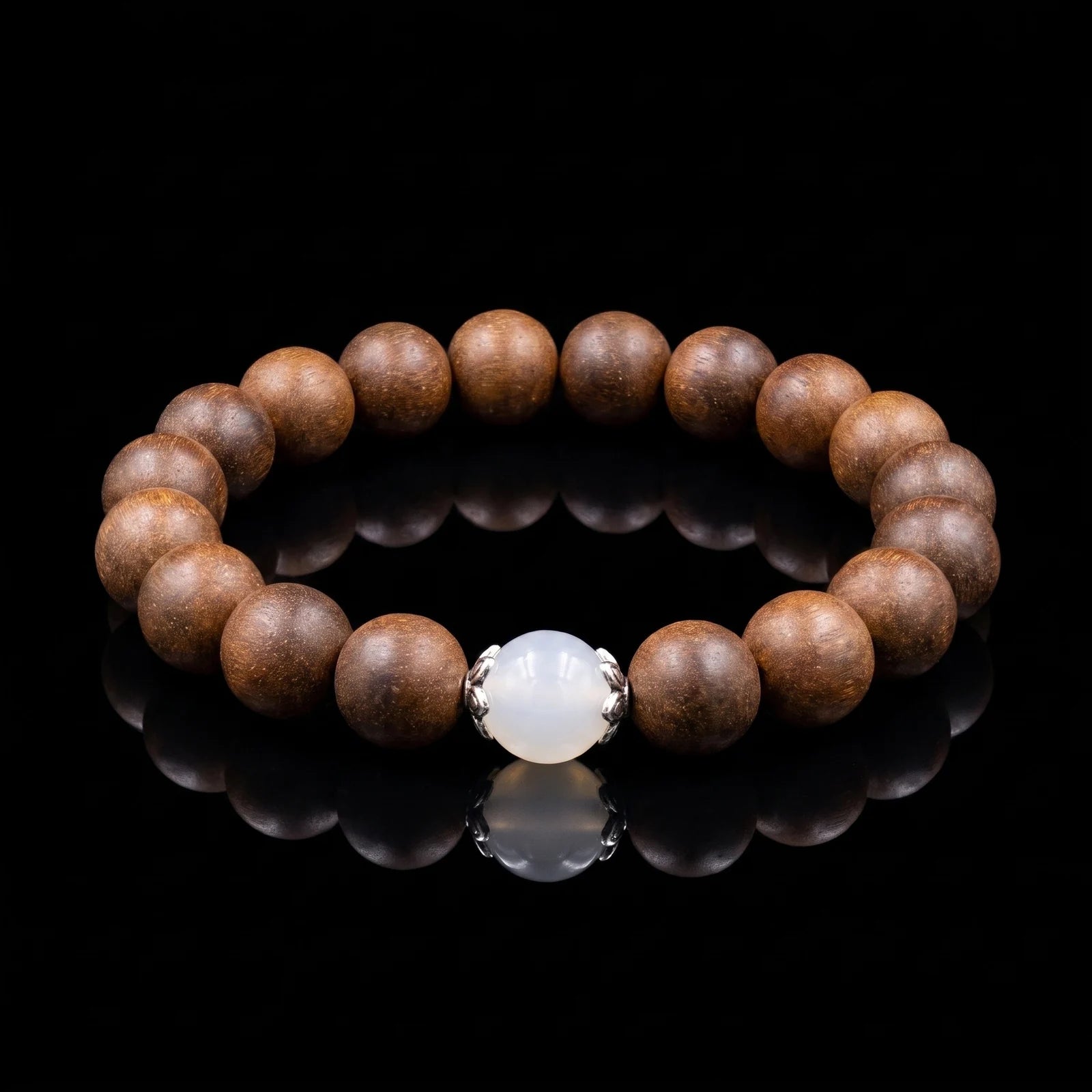 STILL MOON Still Mind wearable incense bracelet with brown aromatic beads and white center bead on a black reflective surface.