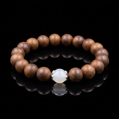 STILL MOON Still Mind wearable incense bracelet with brown aromatic beads and white center bead on a black reflective surface.
