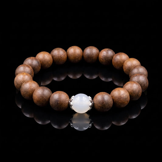 STILL MOON Still Mind wearable incense bracelet with brown aromatic beads and white center bead on a black reflective surface.