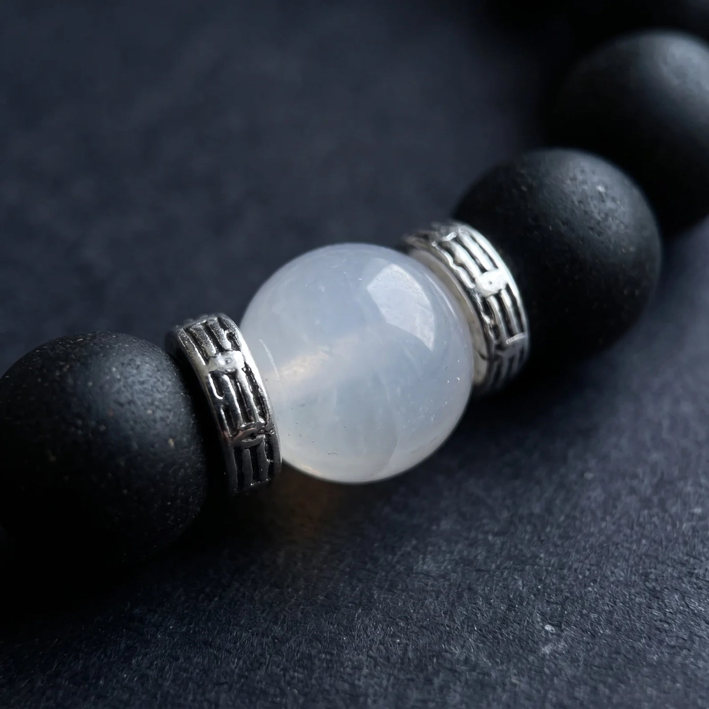 SKIN BREATH bracelet close-up showing black aromatic beads and a white center bead on a dark surface.