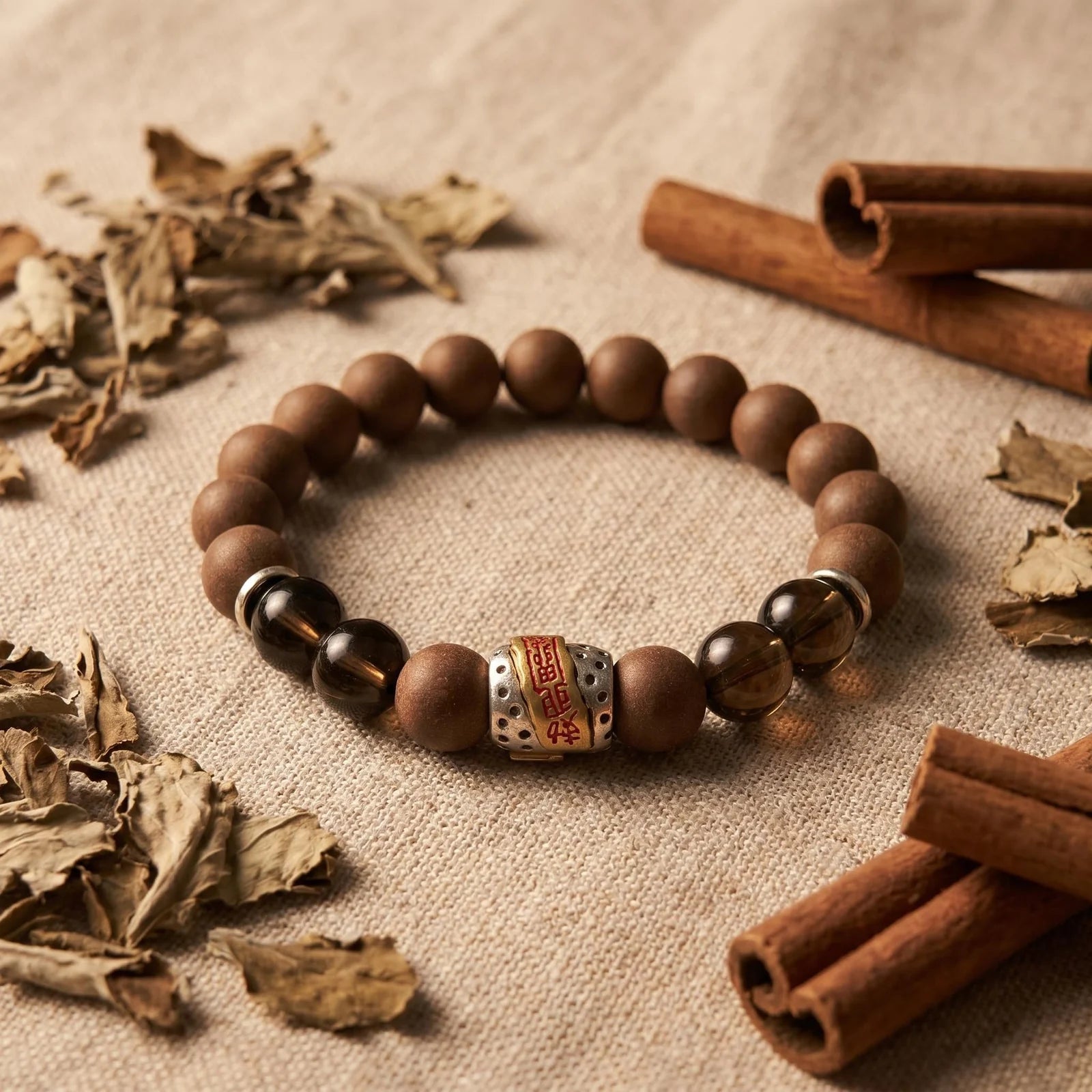 WARM YANG bracelet flat lay with cinnamon and dried herbs for a warm botanical formula story.