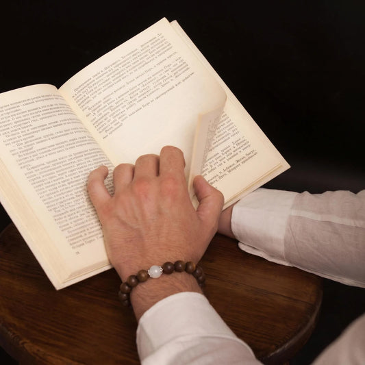 QUIET MOON wearable incense bracelet worn during quiet reading at a dark wooden table.