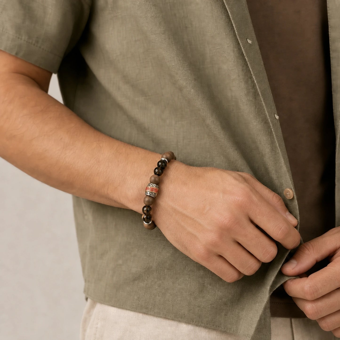 CENSEROOT Warm Ember wearable solid incense bracelet worn with an olive summer overshirt, showing warm brown incense beads, smoky quartz, and a red-gold command-script spacer.